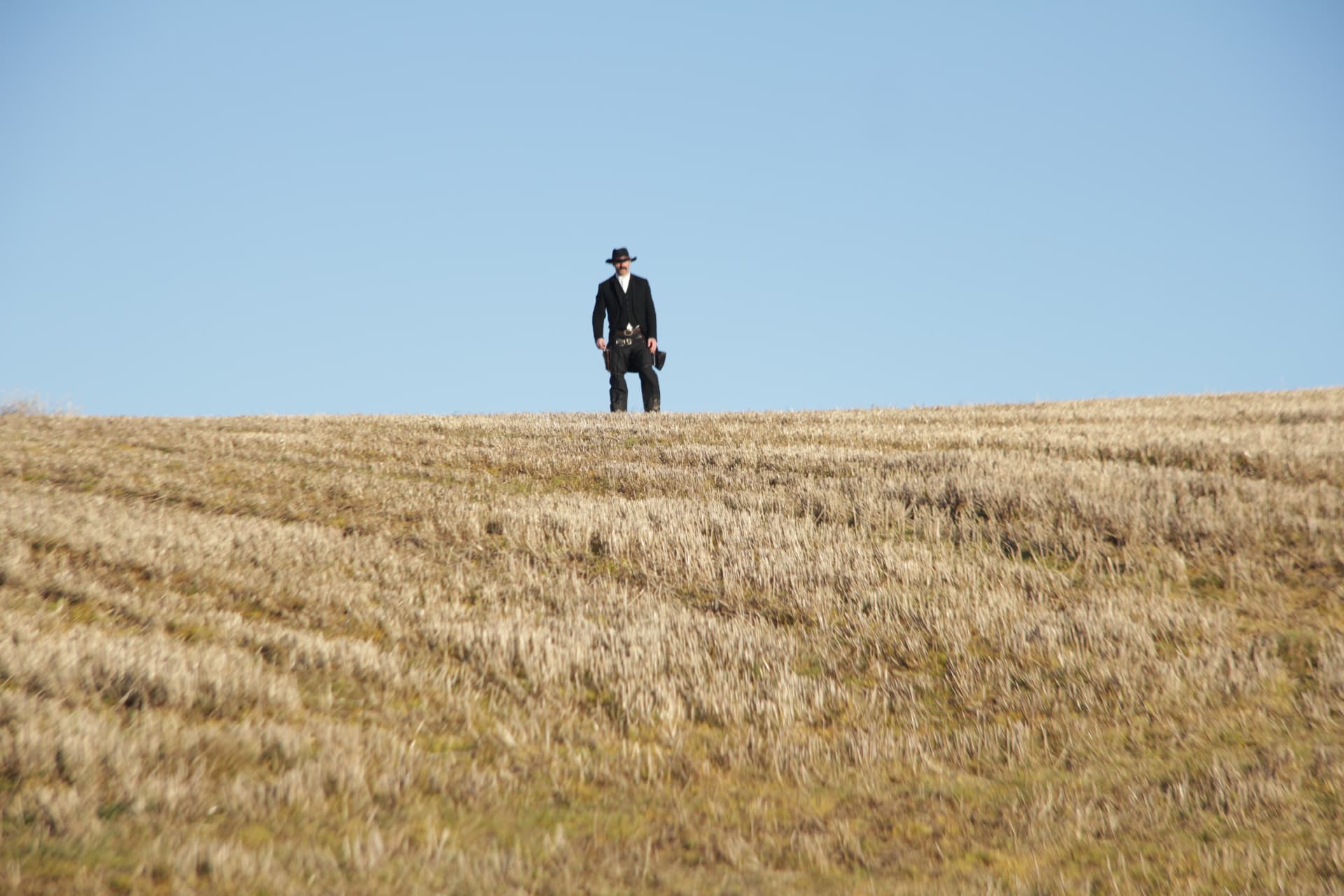 The Stranger walking the ridge of a stubble field during filming