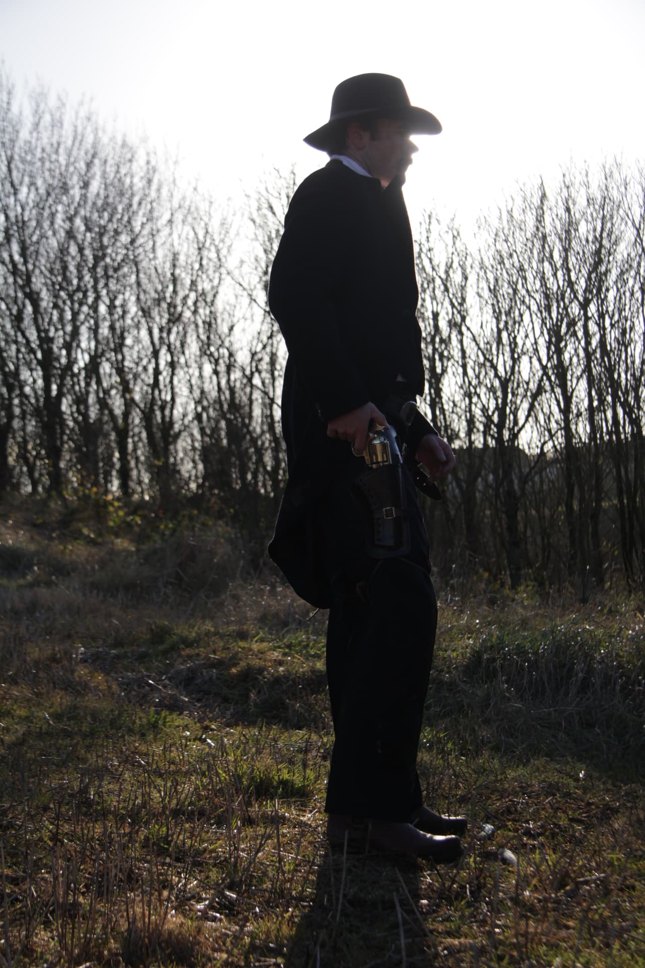 The Stranger drawing his revolver in silhouette against the treeline