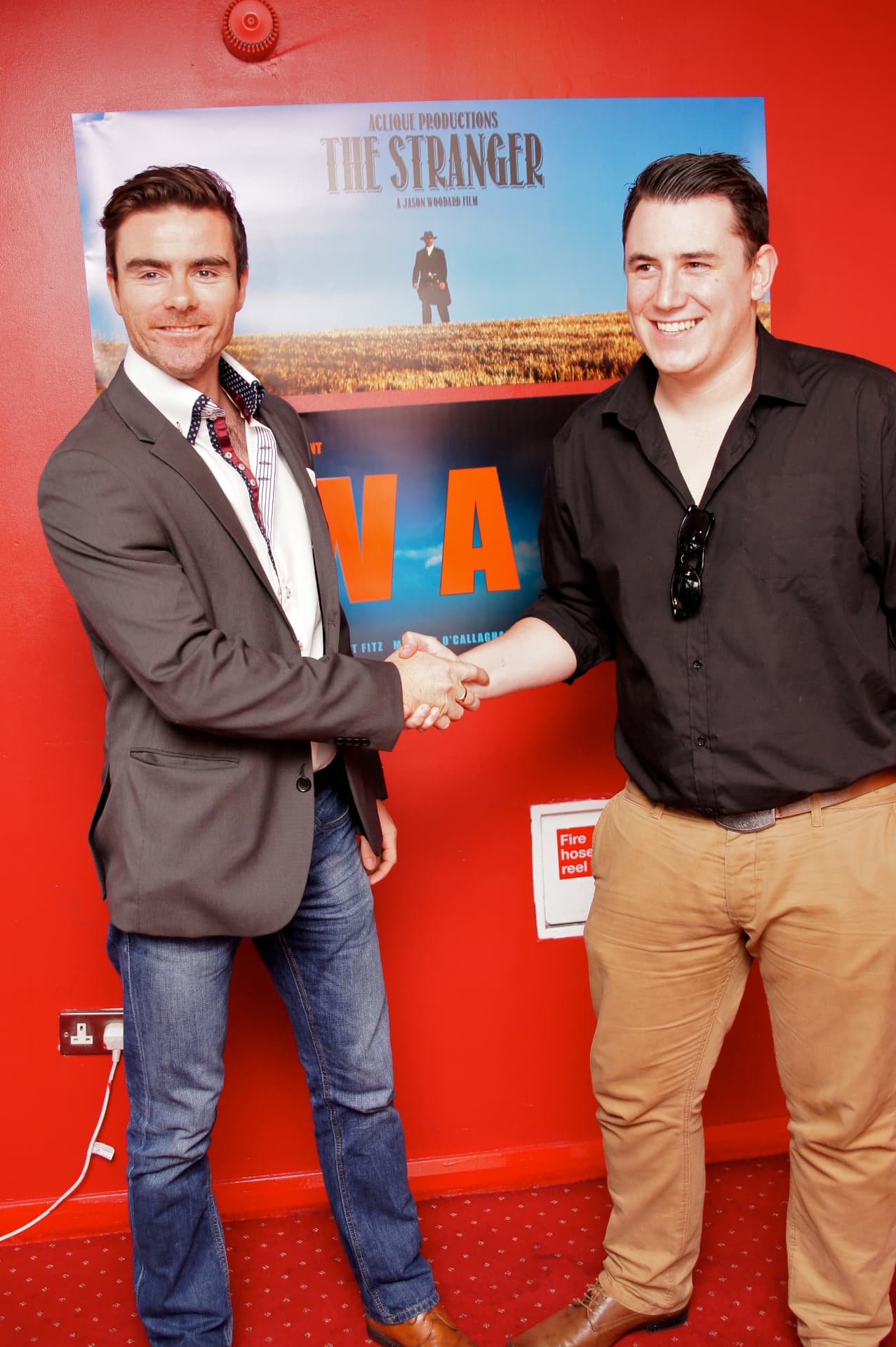 Two filmmakers shaking hands in front of The Stranger poster