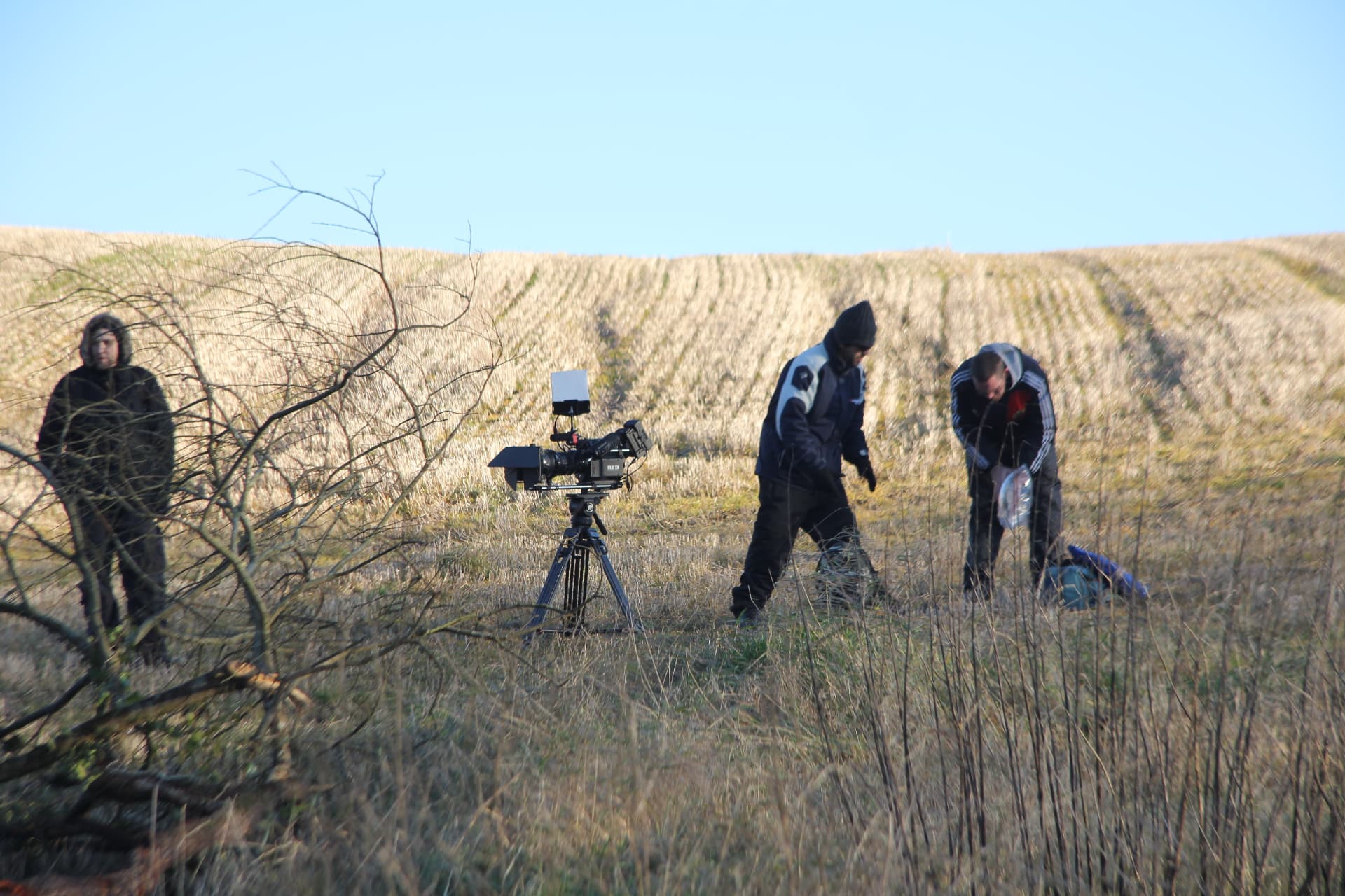 Camera set up on a tripod in the field with crew resetting the shot