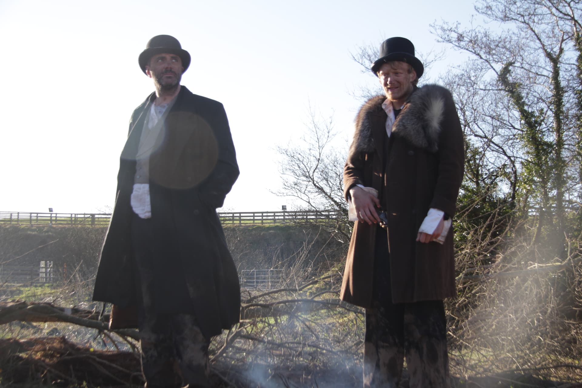 Two actors standing over the smoking bonfire set